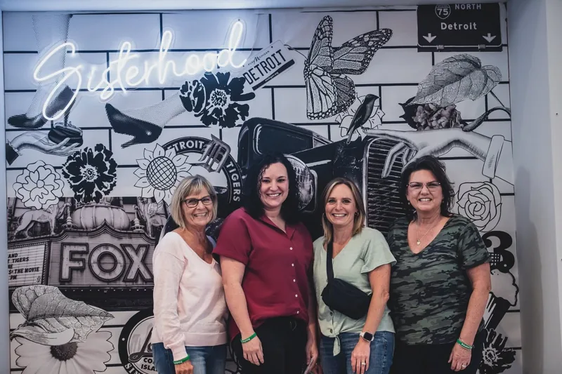 Four women smiling together at a Sisterhood photo wall