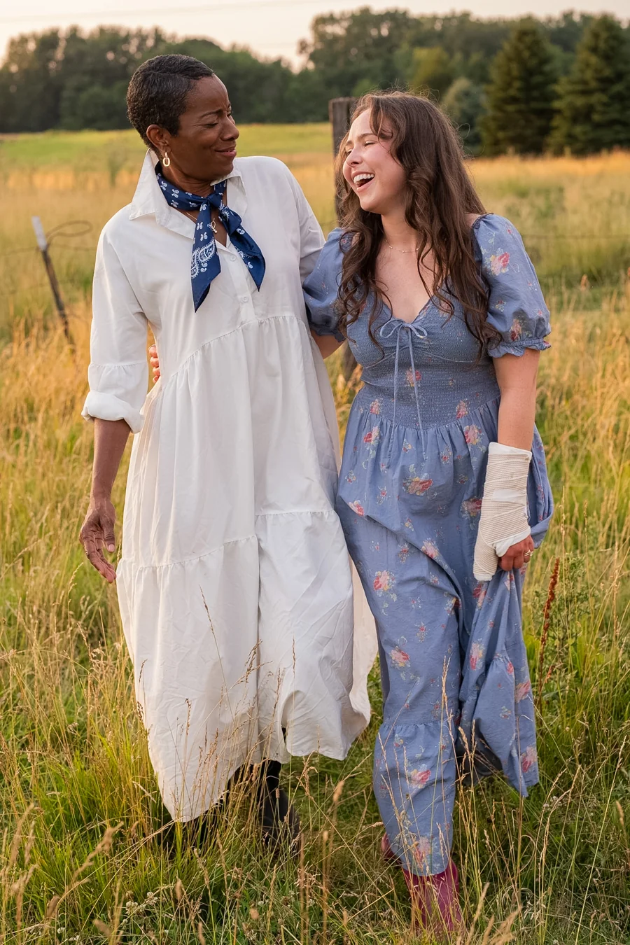 Two women laughing together in a sunlit field at the 2027 Priceless photoshoot